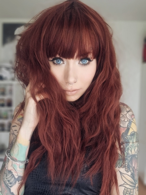 Red long crimped wig with bangs. Babooshka is a rich ruby hue with a dash of paprika from roots to tips. Plenty of volume with invisible layers and a full fringe to peep from under.