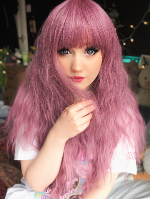 Pink long crimped wig with bangs. Bloom has a deep lilac pink hue from roots to tips. Plenty of volume with invisible layers and a full fringe to peep from under.
