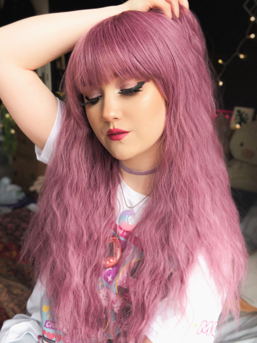 Pink long crimped wig with bangs. Bloom has a deep lilac pink hue from roots to tips. Plenty of volume with invisible layers and a full fringe to peep from under.