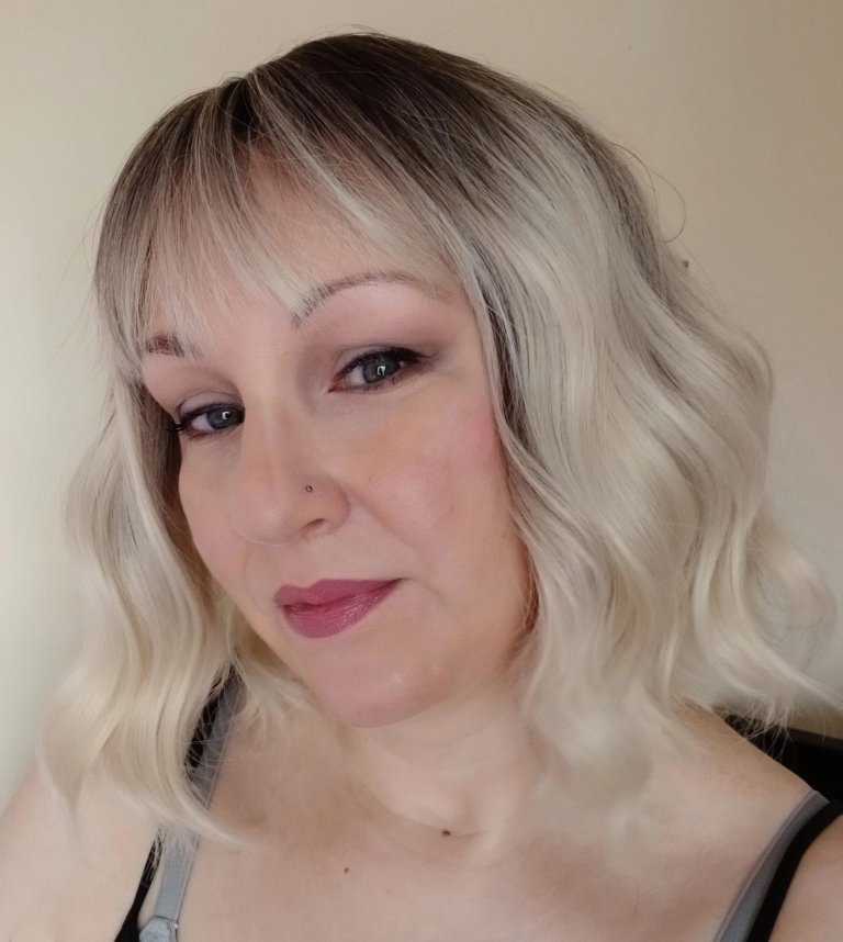 A wig with brown shadowed roots that grow into this platinum blonde icy hue. Styled into a bob with loose waves. The fringe is sleek and blunt.