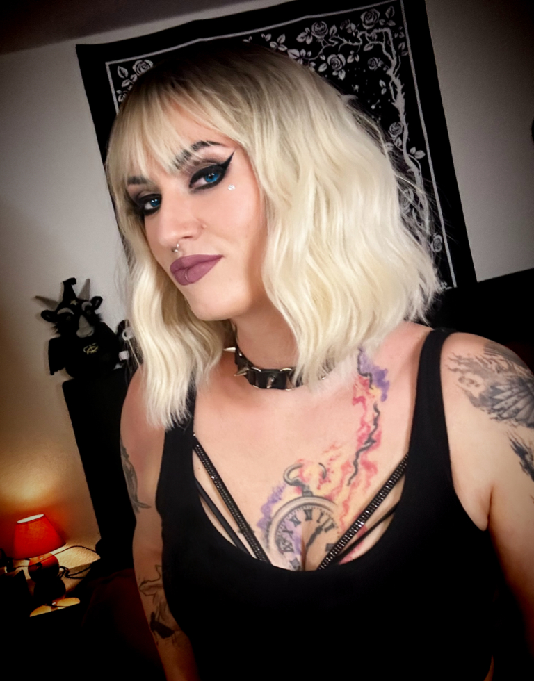 A wig with brown shadowed roots that grow into this platinum blonde icy hue. Styled into a bob with loose waves. The fringe is sleek and blunt.