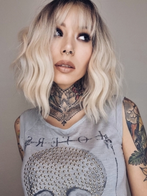 A wig with brown shadowed roots that grow into this platinum blonde icy hue. Styled into a bob with loose waves. The fringe is sleek and blunt.