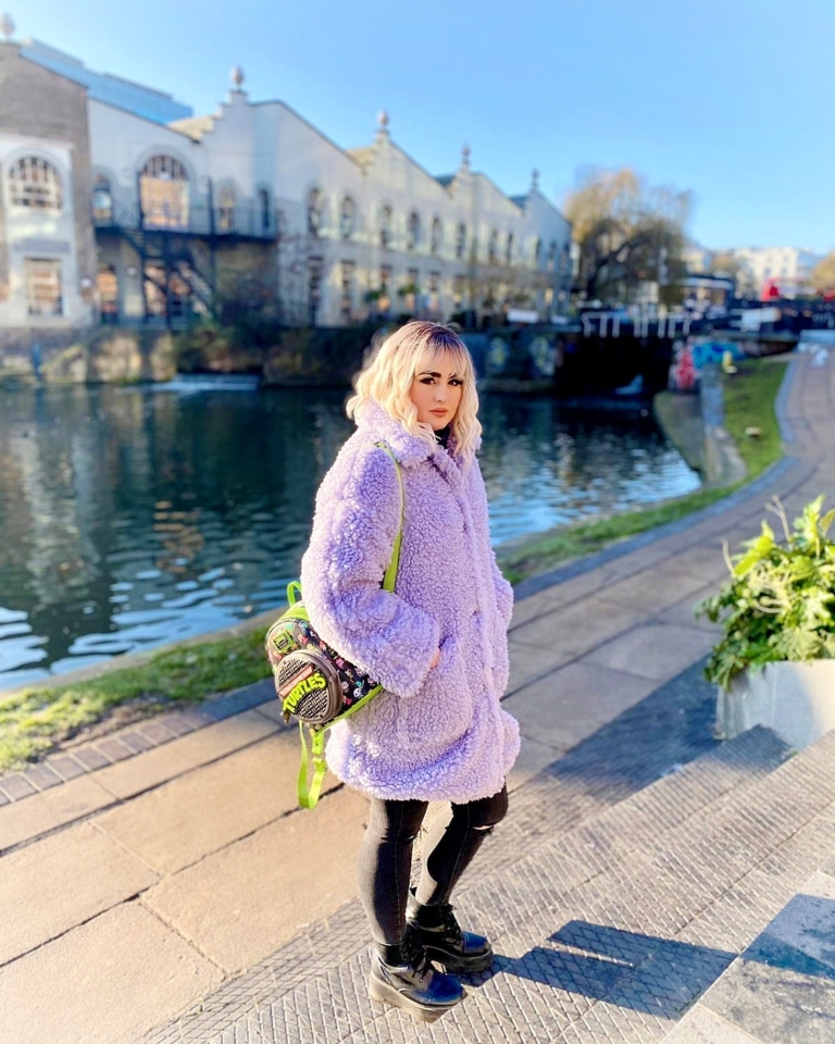 A wig with brown shadowed roots that grow into this platinum blonde icy hue. Styled into a bob with loose waves. The fringe is sleek and blunt.