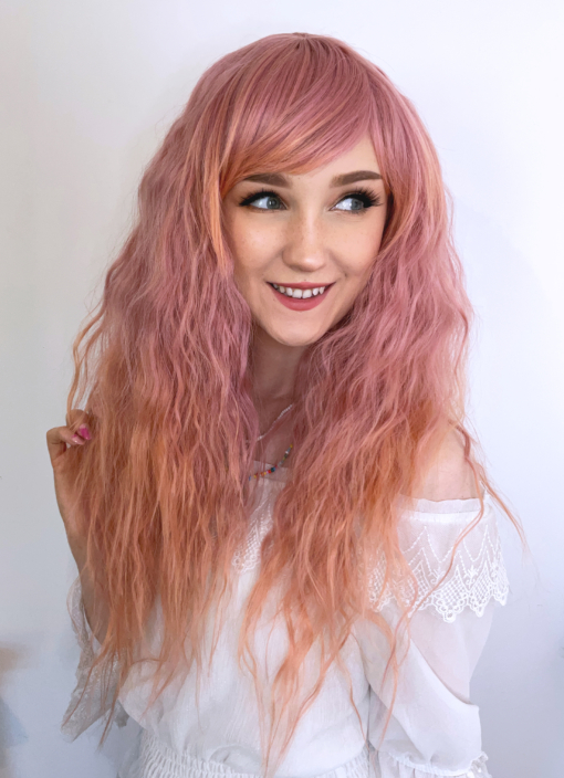 This wig is so fluffy, yet so lightweight and comfortable. A soft crimped style in a blend of coral pink that fades into a more warm-toned peach. The longer fringe allows the freedom to choose between straight across bangs or more of a side fringe. An absolute dream wig!