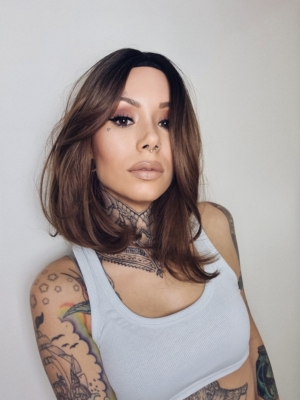 Natural dark brown shadowed roots blend into a warm light brown tone. This fringeless long bob (lob) with two layers each side of the face. Is sleek with a whisper of a wave that curls under.