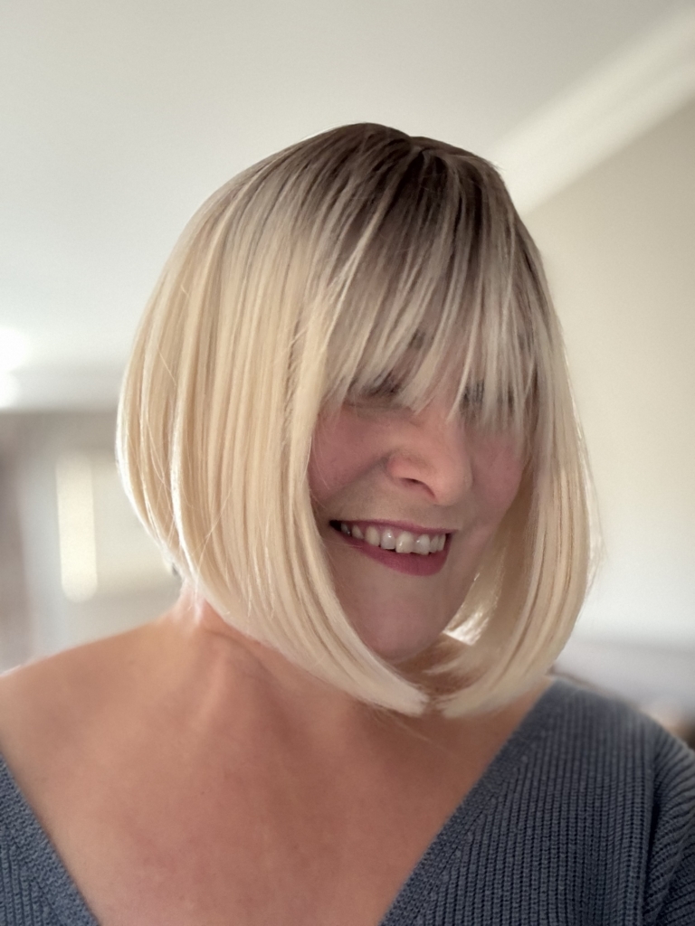 Atonia - Lush Wigs UK This platinum blonde wig has dark brown shadowed roots for a natural feel. Styled sleek that slightly curls under at the ends. Cut into a jaw skimming bob with a sleek blunt fringe.