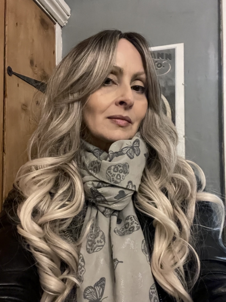 Storm - Lush Wigs UK A mix of dark brown and blonde sleek roots that blend into a sandy blonde colour. It is styled in big loose curls. The sleek long fringe is versatile to be worn to suit your look.