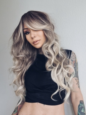 A mix of dark brown and blonde sleek roots that blend into a sandy blonde colour. It is styled in big loose curls. The sleek long fringe is versatile to be worn to suit your look.