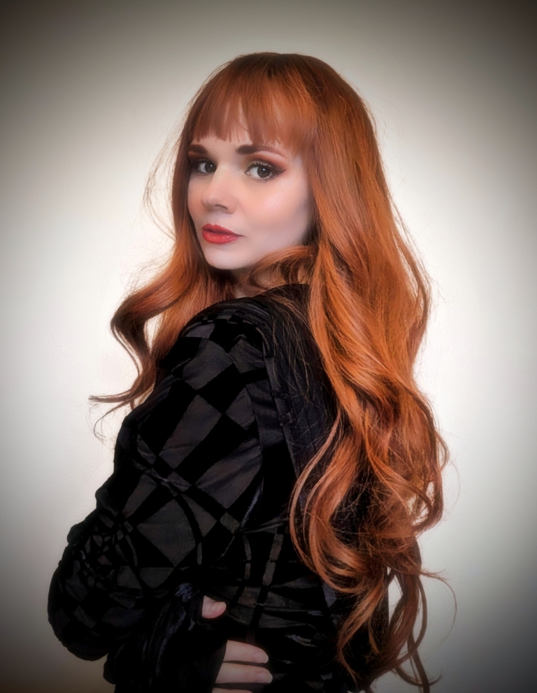 This wig has brown shadow roots that blend into a natural muted auburn colour. Styled in loose barrel curls falling to the waist. The fringe is sleek and blunt.