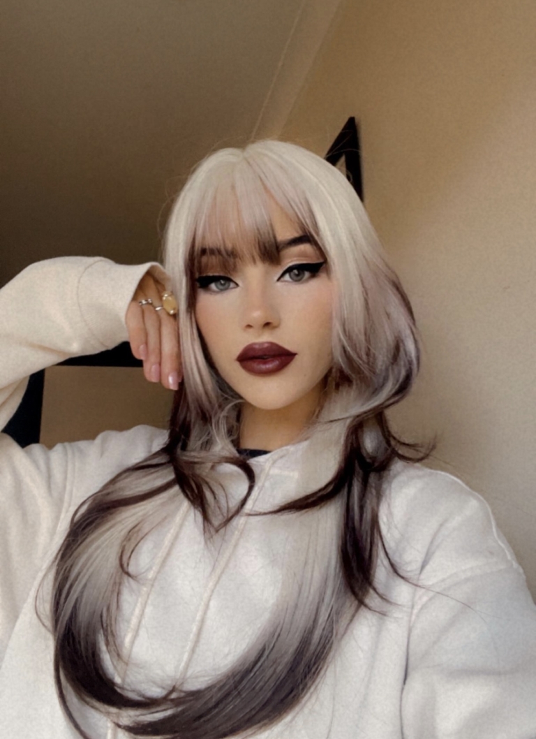 This natural wig comes in a mix of light blonde roots. They blend into a warm brown hue for a dip dye effect on the ends. A sleek long style with long layers at the back, face framing layers at the front make this style easy to maintain. With a sleek blunt fringe finishes the look.