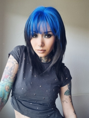This glam rock throwback shaggy cut sleek style has blue roots and a full blue fringe. Cool black tone with a peek a boo of blue from the nape of the neck.