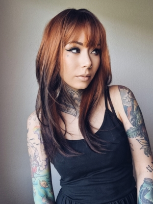 This natural wig with dark brown roots blend into this ginger hue with dark brown tips. A sleek long style with long layers at the back, face framing layers at the front make this style easy to maintain. A blunt sleek fringe frames the face.