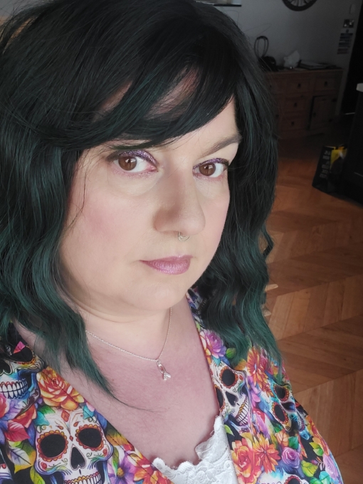 A dark forest green wig with dark brown shadowed roots. Styled into a bob with loose waves and a sleek blunt fringe.