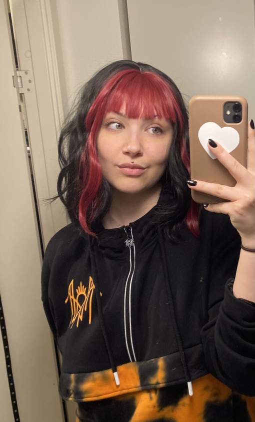 This wavy bob comes to life with a face framing slice of bright purple colour. Thats carried into the sleek fringe and adds a peek-a-boo at the sides. A soft black colour from roots to tips.