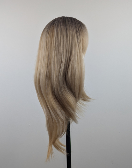 A long and sleek wig with natural dark brown shadowed roots. They blend into a honey blond with sterling blonde highlights. Styled into sleek long layers and a long fringe that can swept to the side or parted into curtain bangs.