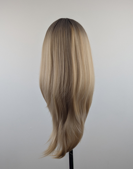 A long and sleek wig with natural dark brown shadowed roots. They blend into a honey blond with sterling blonde highlights. Styled into sleek long layers and a long fringe that can swept to the side or parted into curtain bangs.