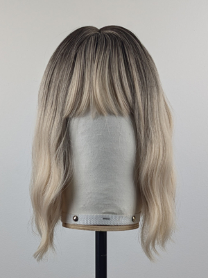 A wig with brown shadowed roots that grow into this platinum blonde icy hue. Styled into a bob with loose waves. The fringe is sleek and blunt.