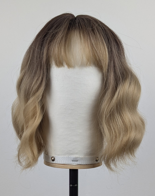 This bob is coloured in a honey blonde tone with brown shadowed roots. That gives a natural feel to the look. A loose wave and a sleek fringe finishes the look.