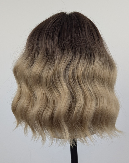 This bob is coloured in a honey blonde tone with brown shadowed roots. That gives a natural feel to the look. A loose wave and a sleek fringe finishes the look.