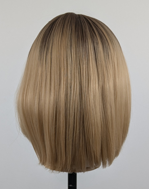 This sandy natural blonde wig is simple and chic. Brown shadowed roots melt into a blonde hue with sun-kissed tips that create the perfect shades for a natural look. A straight one-length bob that curls under at the ends.