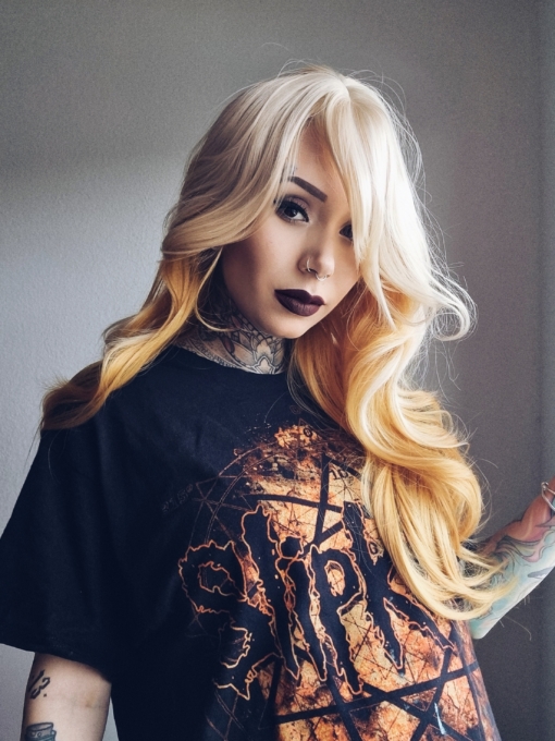 A light blonde colour from crown of the head and the fringe. Underneath is a soft natural ginger sunshine hue. Styled sleek and long into waves throughout the lengths of the hair with cut in layers. A blunt fringe frames the face.