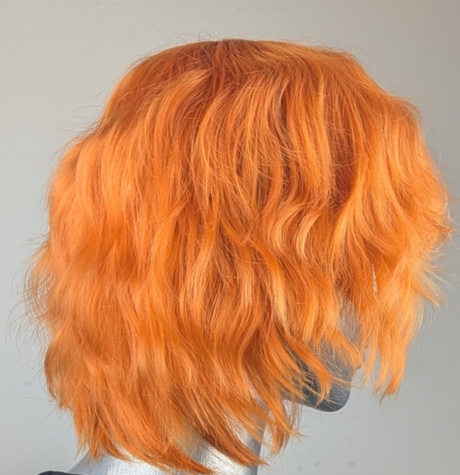 A cute pixie cut in a clementine orange colour. Sleek short layers are blow dried with a large barrel brush. Wear it forward or swept to the side away from the face.