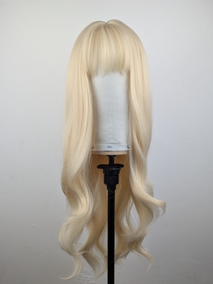 This wig has a light golden blonde colour from roots to tips. It’s styled sleek with large blow out curls at the ends for volume. A sleek blunt fringe frames the face.