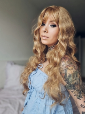 Aurelia - Lush Wigs UK This natural wig comes in a mix of caramel blonde from roots to tips. A Voluminous curly style, cut into face framing layers at the front. With a sleek blunt fringe that finishes the look.