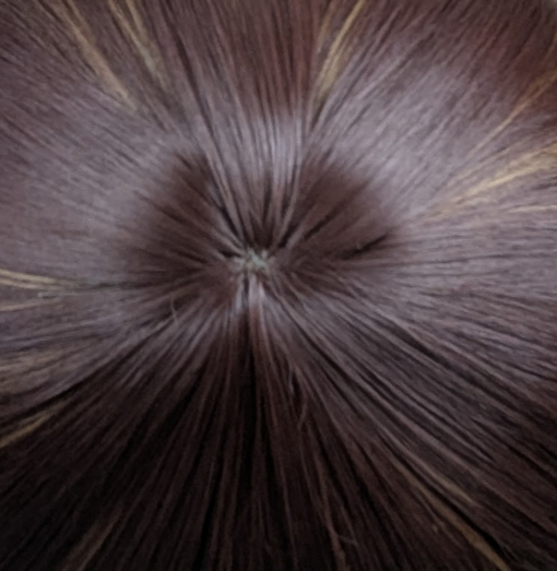 A warm brown wig with golden blonde highlights throughout. Styled into a long bob thats sleek from the roots, ending in large curls. The full blunt fringe is sleek.