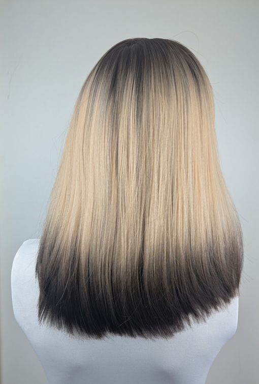 This natural wig is simple but its twist on colour adds some dimension. A sleek long bob (lob) with a light blunt fringe. Dark brown shadowed roots blend into this light blonde colour, finished with a block of dark brown at the tips. A natural mix of colour that sets this look.