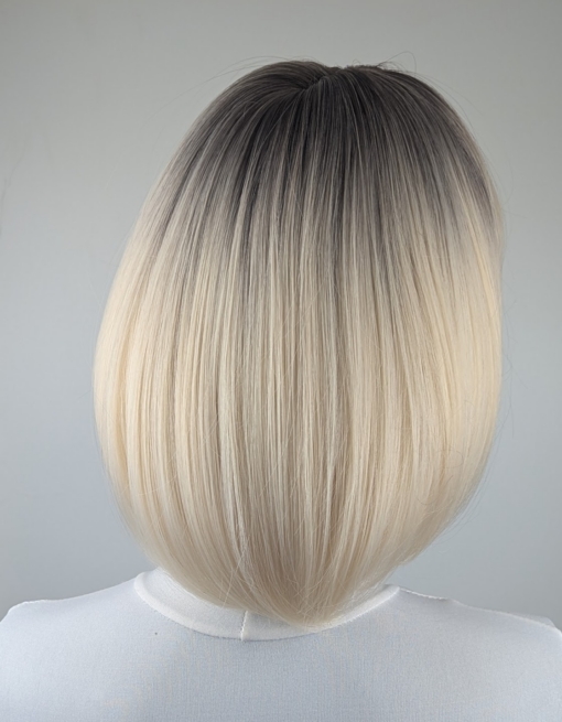 Atonia - Lush Wigs UK This platinum blonde wig has dark brown shadowed roots for a natural feel. Styled sleek that slightly curls under at the ends. Cut into a jaw skimming bob with a sleek blunt fringe.