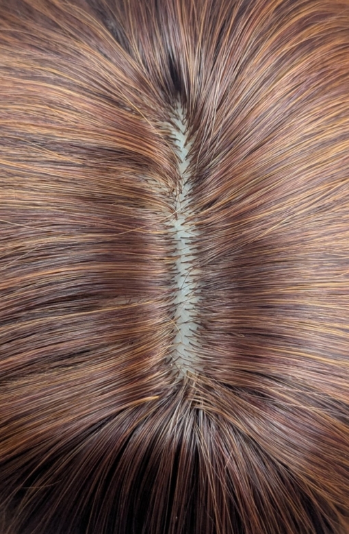 This wig has brown shadow roots that blend into a natural warm mix of copper and auburn tone. Styled in loose barrel curls falling to the waist. The fringe is sleek and blunt.