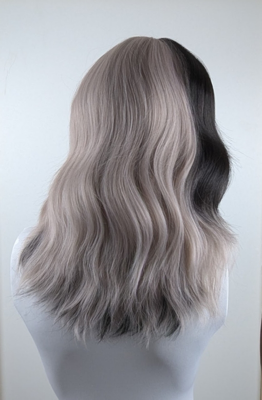 Eclipse - Lush Wigs UK Sterling blonde with a mix of grey. A slice of jet black for added definition takes this style to the next level. Black tones come from the nape of the neck. Giving a peek-a-boo effect. Loose waves fall just past the shoulders, a blunt sleek fringe carries the split colour.