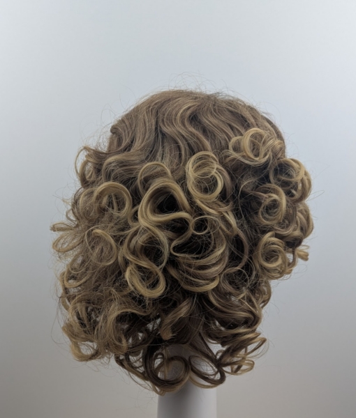 This curly fringe-less short-bob has natural brown shadow roots that blend into honey blonde tight curls. Shake it up into an 80s inspired look. Or tone it down for a vintage 30s look. 