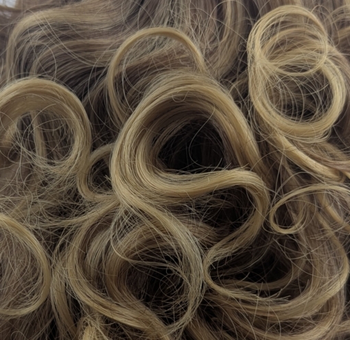 This curly fringe-less short-bob has natural brown shadow roots that blend into honey blonde tight curls. Shake it up into an 80s inspired look. Or tone it down for a vintage 30s look. 
