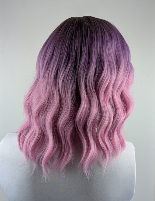 This wig has brown shadowed roots that melt into a dark lilac colour into a soft pink ombre. A bob styled into loose waves with a sleek blunt fringe.