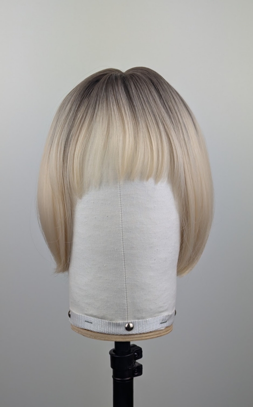 Outlet #255 - Lush Wigs UK This platinum blonde wig has dark brown shadowed roots for a natural feel. Styled sleek that slightly curls under at the ends. Cut into a jaw skimming bob with a sleek blunt fringe.