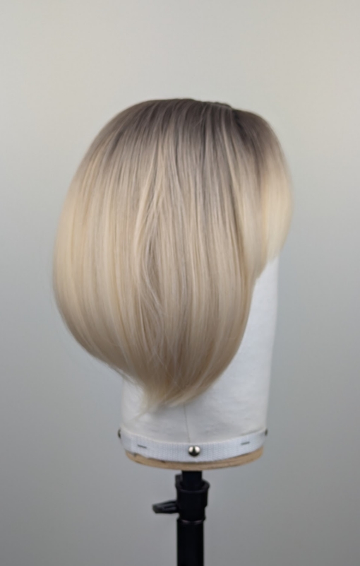 Outlet #255 - Lush Wigs UK This platinum blonde wig has dark brown shadowed roots for a natural feel. Styled sleek that slightly curls under at the ends. Cut into a jaw skimming bob with a sleek blunt fringe.