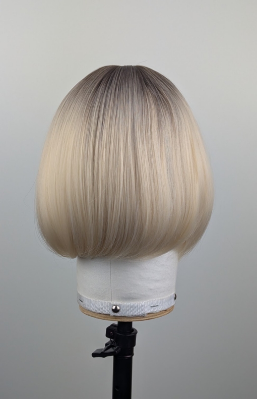 Outlet #255 - Lush Wigs UK This platinum blonde wig has dark brown shadowed roots for a natural feel. Styled sleek that slightly curls under at the ends. Cut into a jaw skimming bob with a sleek blunt fringe.
